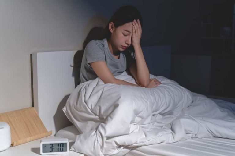 Mulher na cama com a mão no rosto